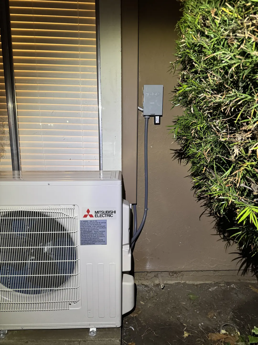 Mitsubishi Electric ductless mini-split outdoor heat pump installed on a Westside Los Angeles side yard with shrub-screened condenser placement and dedicated electrical disconnect