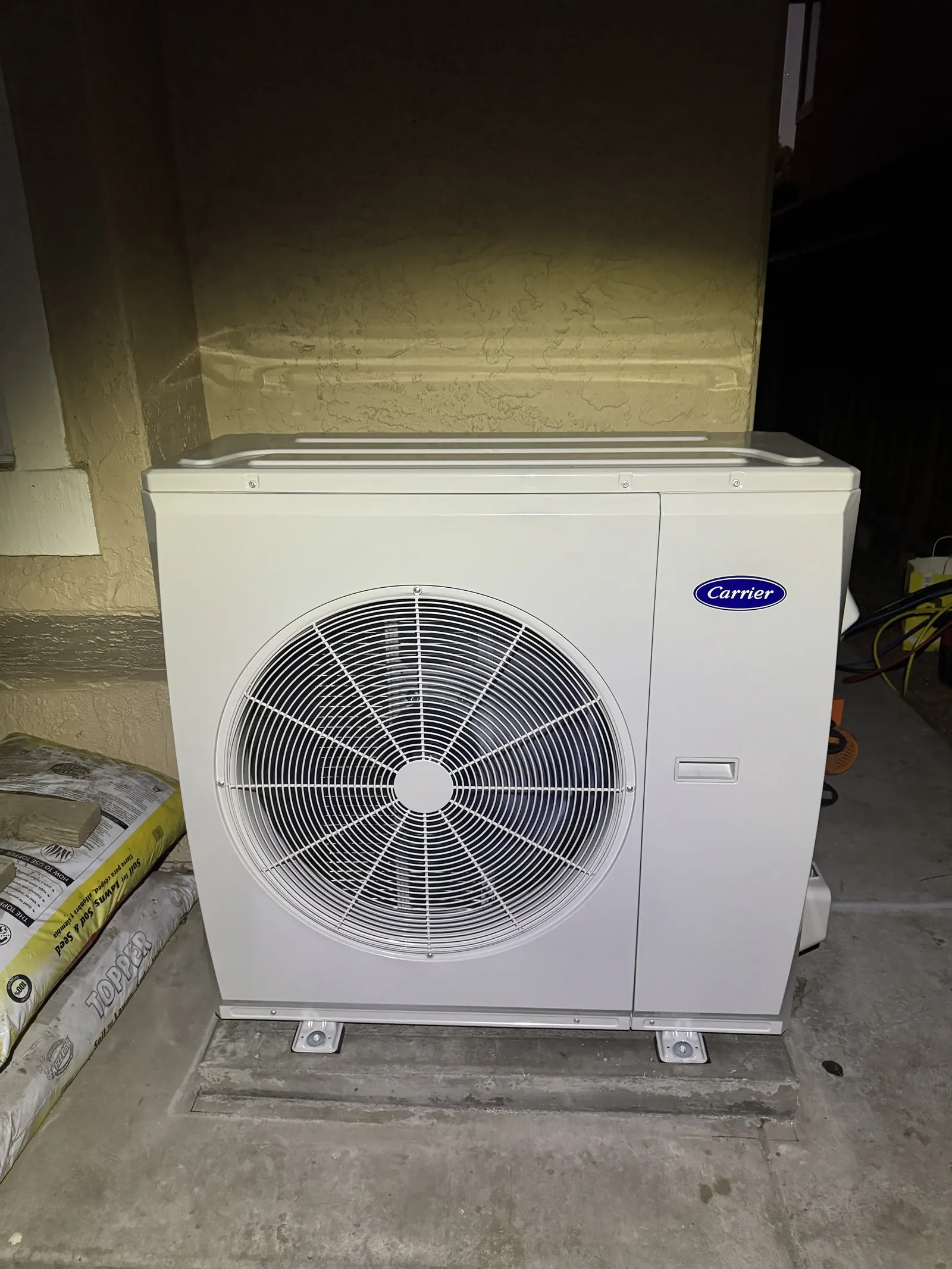 Carrier inverter heat pump outdoor unit installed on a stucco wall pad in a West LA side yard, ready for line-set hookup